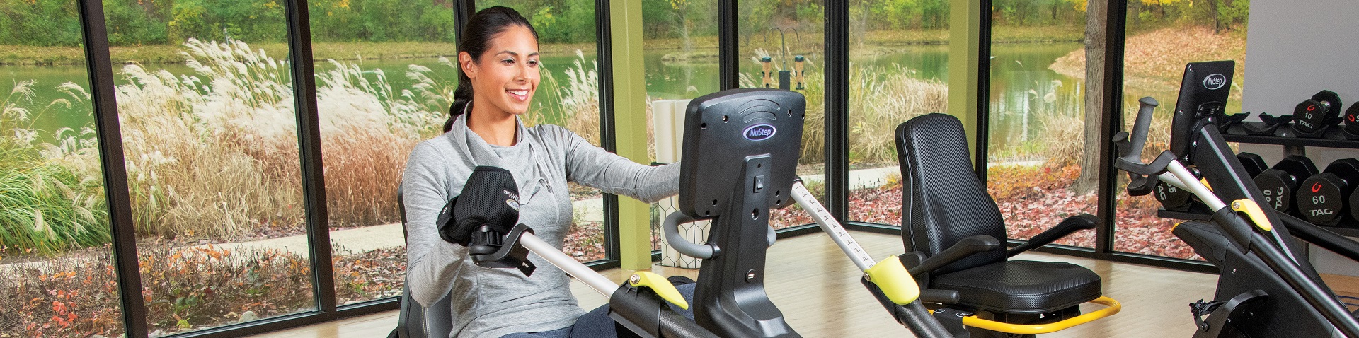 young woman on a NuStep cross trainer in exercise room fall background with pond